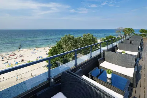 Wygodne fotele i stoliki na tarasie z widokiem na piaszczystą plażę i błękitne morze. Idealne miejsce na relaks, gdy dostępne są wolne pokoje z widokiem na morze.