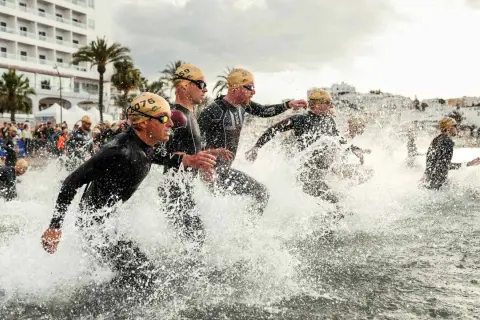 Sportler stürmen ins Wasser für einen Triathlon Kurzdistanz.
