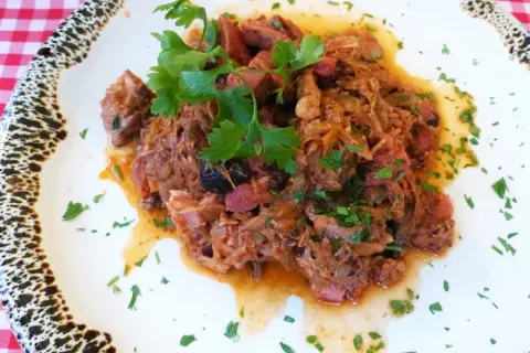 Pyszny bigos z kiszonej kapusty, bogaty w mięso i przyprawy, udekorowany świeżą natką pietruszki.