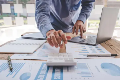 Osoba przy biurku z laptopem, kalkulatorem i dokumentami finansowymi.