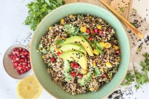 Bunter Quinoa Salat mit Avocado, Granatapfelkernen, Mais und Petersilie, garniert mit schwarzen Sesamkörnchen.