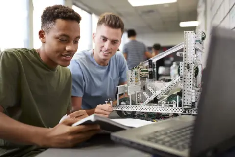 Dos estudiantes trabajan en un robot, aplicando la metodología STEM para resolver un desafío de ingeniería.