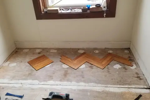 Wooden floor planks laid in a herringbone pattern on a subfloor, tools nearby. This is part of a project on how to level floor.