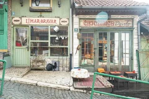 Faszinierende Szene in der Sarajevo Altstadt: Ein Vogel sitzt auf einem Geschäftsschild, davor ein Tisch mit Blumen.
