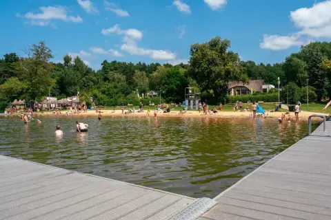 Słoneczny dzień na kąpieliskach w Poznaniu. Ludzie kąpią się, opalają na plaży i odpoczywają nad wodą.