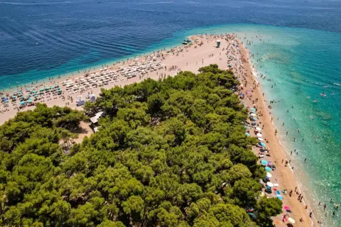En solig strand med många parasoller och badande människor vid Zlatni Rat, en berömd udde på ön Brač i Kroatien.