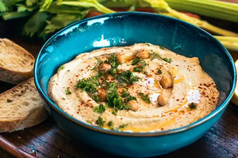 Cremiger Hummus mit Kichererbsen, Petersilie und Paprikapulver in einer blauen Schüssel, serviert mit Brot. Ein köstliches Hummus Rezept.