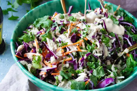 En fräsch kycklingsallad med rödkål, morötter och grönkål, toppad med en krämig dressing. En flaska kycklingfond syns i bakgrunden.
