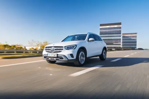 Biały Mercedes GLC 200 jedzie po pustej drodze, w tle nowoczesne budynki biurowe.
