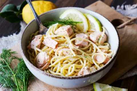 Schüssel mit cremigen Nudeln mit Lachs, garniert mit Zitronenscheiben und Dill. Ein Genuss für Feinschmecker!