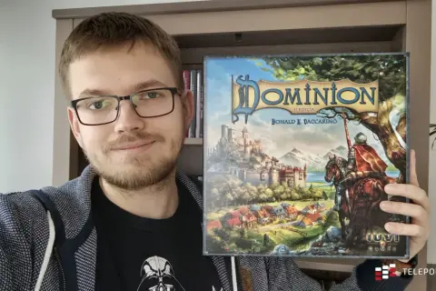 Uśmiechnięty mężczyzna prezentuje pudełko gry "Dominion II Edycja". To dopiero początek przygody z nowymi dodatkami!