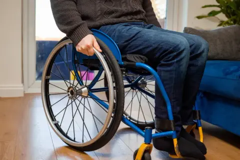 Osoba na wózku inwalidzkim, która może skorzystać z programu 500 plus dla niepełnosprawnych, siedzi na drewnianej podłodze.