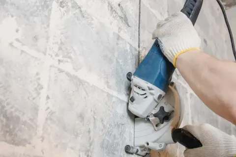 Mani guantate usano una fresatrice per creare tracce nel muro senza polvere, un lavoro di precisione.