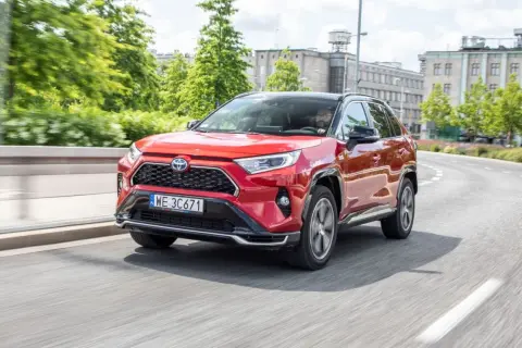 Czerwona Toyota RAV4 Hybrid w ruchu miejskim. Kierowca w okularach za kierownicą. Niskie toyota rav4 spalanie to atut tego SUV-a.