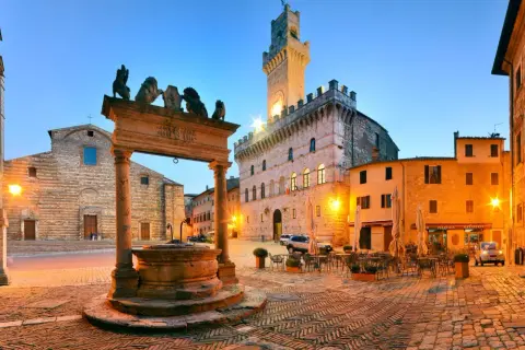 Piazza illuminata a Montepulciano, con pozzo rinascimentale, Palazzo Comunale e chiese. Perfetta per scoprire le cose da fare in zona.
