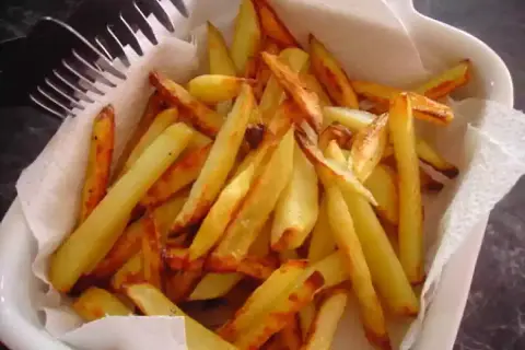 Un plat blanc rempli de délicieuses frites au four, dorées et croustillantes, prêtes à être dégustées. Une fourchette est posée sur le bord.