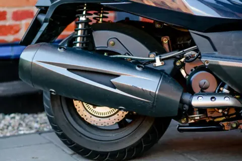 Zbliżenie na tylne koło i wydech ciemnego motocykla.