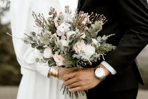 Un bouquet de mariée, roses pâles et feuillage, tenu par un couple. Peut-être une allusion à pourquoi on ne se marie pas en mai.