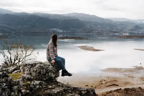 Frau sitzt auf Felsen mit Blick auf einen See und Berge. Ein perfekter Moment während eines Montenegro Roadtrips.
