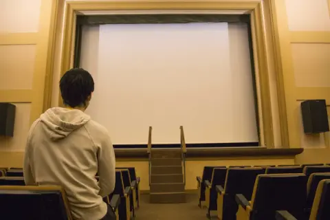 Un joven espera en un cine vacío, listo para disfrutar de una película.