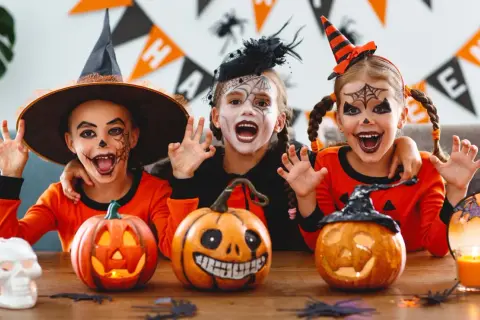 Tre barn med läskig ansiktsmålning och halloween-kostymer njuter av en halloween fest med pumpor och dekorationer.