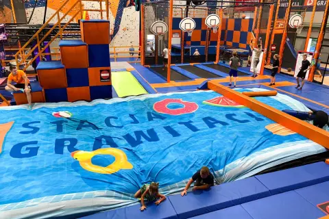 Wesołe skakanie na trampolinach w centrum rozrywki dla dorosłych. Dzieci i młodzież bawią się na wielkiej, niebieskiej macie z motywem basenu.