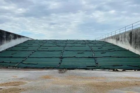 Ampia trincea agricola coperta da telo verde, con pareti in cemento e cielo nuvoloso.