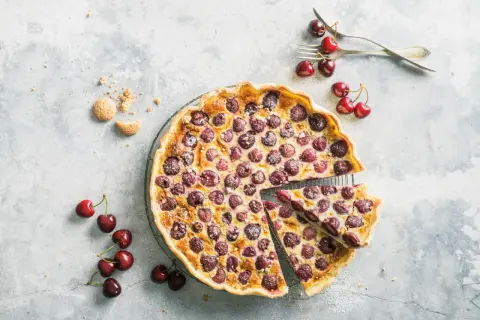 Tarte aux cerises à l'ancienne, garnie de fruits rouges juteux et saupoudrée de sucre glace. Une part est déjà servie.