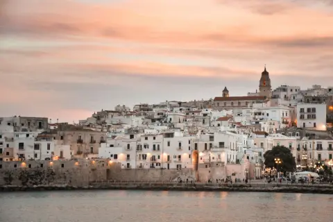 Vieste lungomare al tramonto, con case bianche aggrappate alla collina e il mare calmo.