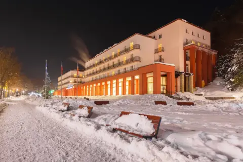 Zimowy wieczór w sanatorium godnym polecenia. Ośnieżone ławki i drzewa tworzą bajkową scenerię.