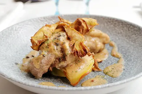Delicioso ternasco a la pastora, tierno cordero bañado en una rica salsa, coronado con crujientes alcachofas fritas.