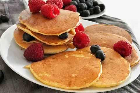 Gestapelte, goldbraune, gesunde Pancakes mit frischen Himbeeren und Blaubeeren garniert. Ein köstlicher Start in den Tag.