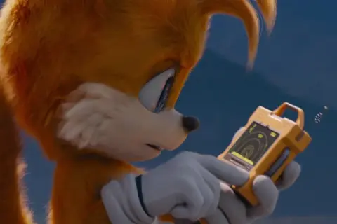 Tails Sonic, z dwoma ogonami, analizuje dane na żółtym urządzeniu.