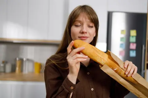 Kobieta wącha świeżą bagietkę, zastanawiając się, jakie choroby powoduje gluten.