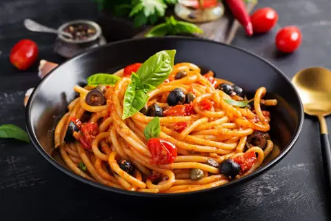 Un plat de pâtes aux anchois, tomates, olives et câpres, garni de basilic frais. Un délice méditerranéen.