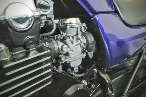 Fragment motocykla z widocznym gaźnikiem i elementami silnika.