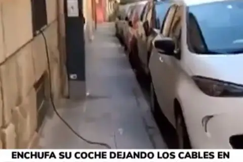 Un coche eléctrico en carga, con cables cruzando la acera, obstaculizando el paso.