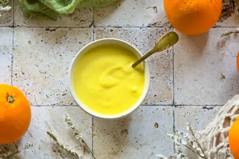 Crema gialla e liscia in una ciotola, con arance fresche intorno. Un cucchiaio dorato è immerso nella crema, che ricorda il sapore del sale all'arancia.