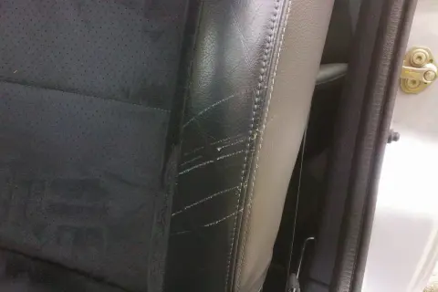 Siège de voiture en cuir noir avec des éraflures visibles, nécessitant une réparation de griffure cuir.