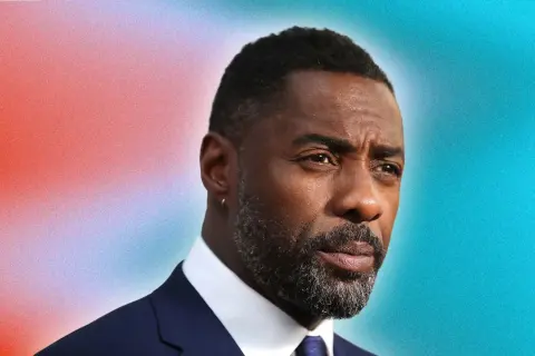 Idris Elba arbore une barbe grise stylée, un modèle barbe dégradé impeccable, sur fond dégradé rouge et bleu.