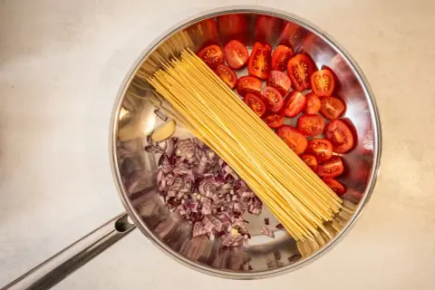 Zutaten für ein schnelles One-Pot-Gericht: Spaghetti, gehackte rote Zwiebeln, Kirschtomaten und Knoblauch in einer Pfanne.