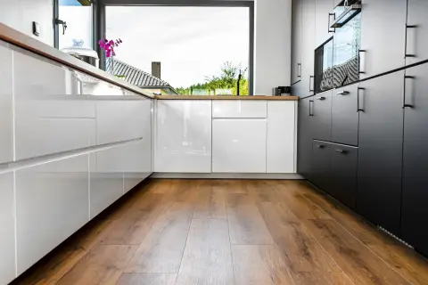 Cuisine moderne avec des armoires blanches et noires brillantes, un grand évier et un parquet au sol chaleureux.