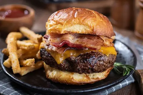 Gros plan sur un burger maison avec bacon, fromage fondant et frites croustillantes sur une assiette noire.