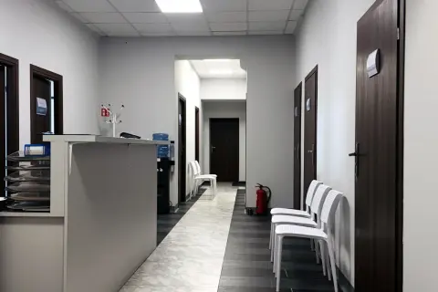 Korytarz centrum medycznego z recepcją, drzwiami i białymi krzesłami.