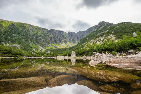 Spokojne, górskie jezioro odbija skaliste zbocza i chmury. To widok z najkrótsza trasa do Śnieżnych Stawków.