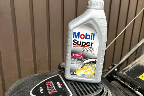 Butelka oleju Mobil Super 2000 10W-40 na silniku kosiarki Briggs & Stratton.