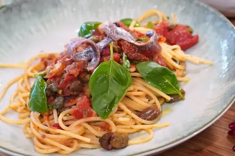 Spaghetti Puttanesca mit Sardellen, Oliven, Kapern und frischem Basilikum auf einem Teller.