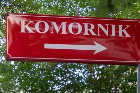 Czerwony znak drogowy z napisem "KOMORNIK" i białą strzałką w prawo. Może symbolizować drogę do komornika, gdy umowa zlecenie jest zagrożona.