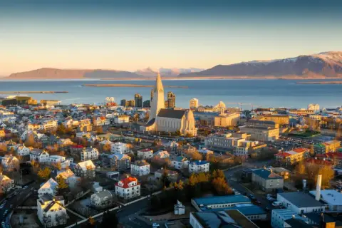 Fakta om Island: Reykjaviks ikoniska kyrka Hallgrímskirkja reser sig över staden med havet och snöklädda berg i bakgrunden.