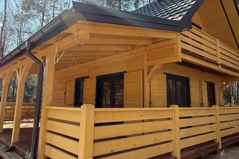 Nowoczesne budownictwo drewniane w Polsce. Dom z bali z werandą i balkonem, otoczony lasem.